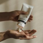 Close-up of a woman squeezing lotion onto her hand, emphasizing skincare and self-care routine.